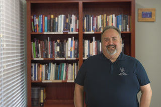 Marc Hinds smiling and standing in front of a bookshelf